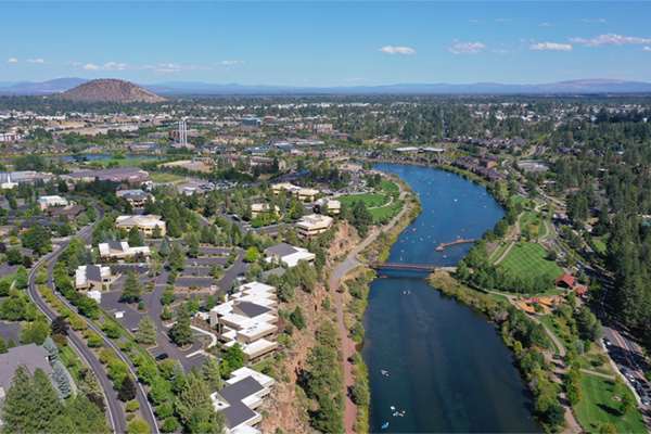 Drone shot of Deschutes River looking east towards the Old Mill District. Pilot Butte in the background. Partly cloudy blue skies.