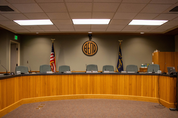 Council Chambers. Dieses with wood front, green chairs behind, light brown wall with City of Bend logo on it in the background.