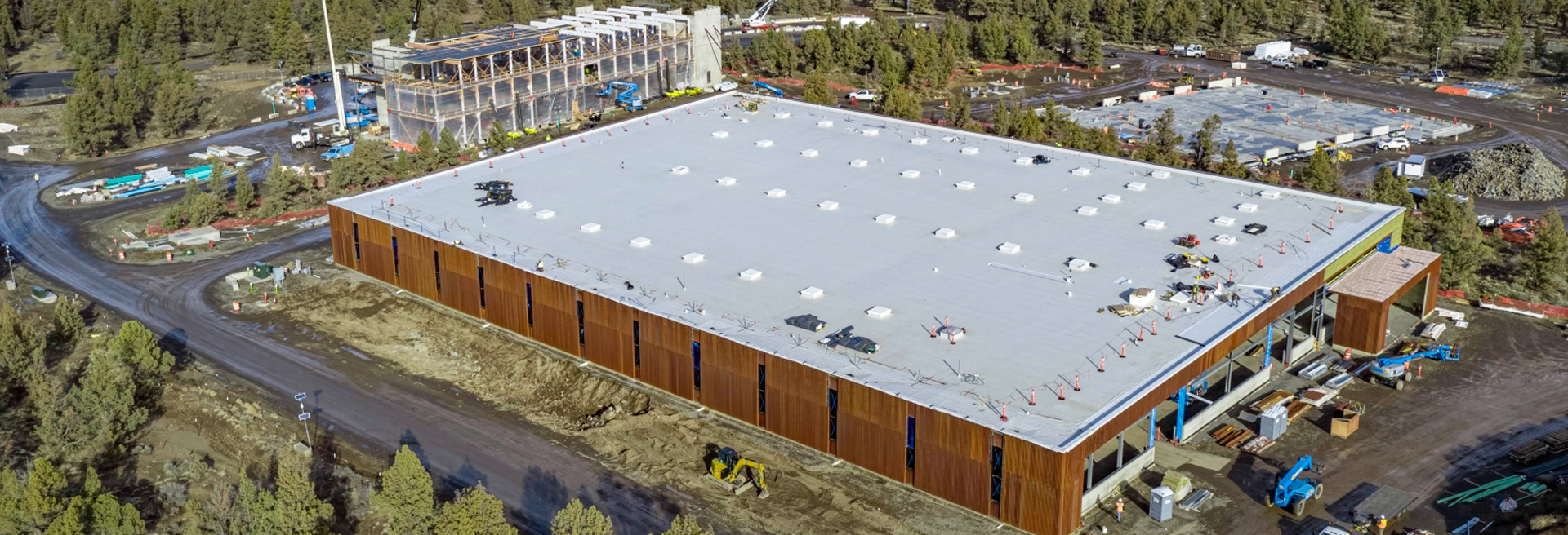 Overhead view of new campus, buildings with white roofs, brown exterior. Surrounded by Juniper Trees and roads.