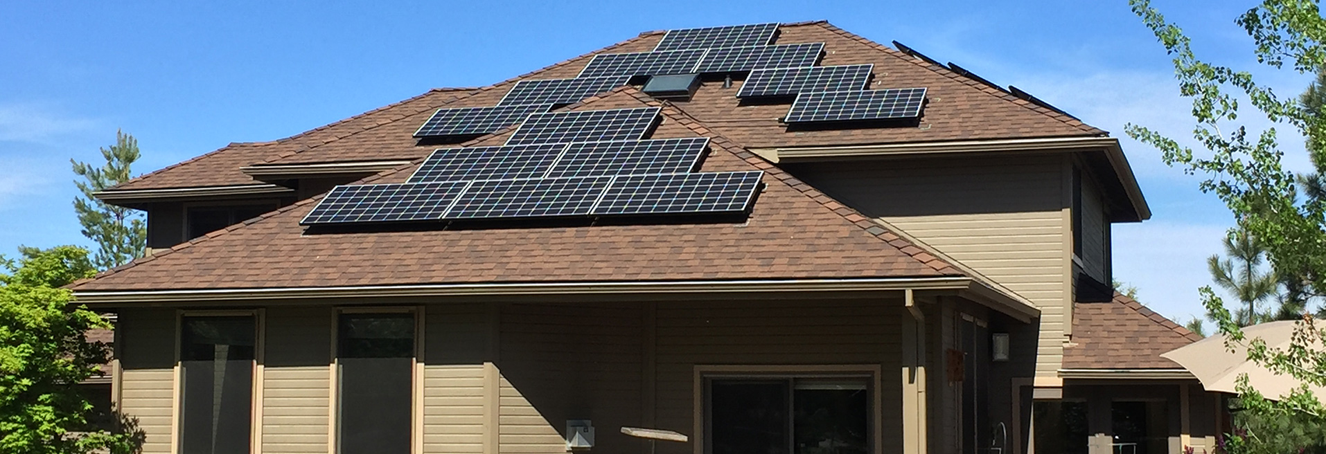Solar Panels on top of a residence. Blue sky in the background. Home is brown in color.