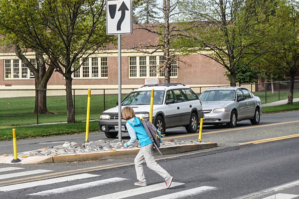 Child crossing a crosswalk on a street with a car waiting.