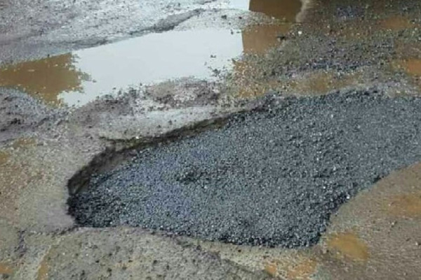 Pothole on a street with water puddles around it.
