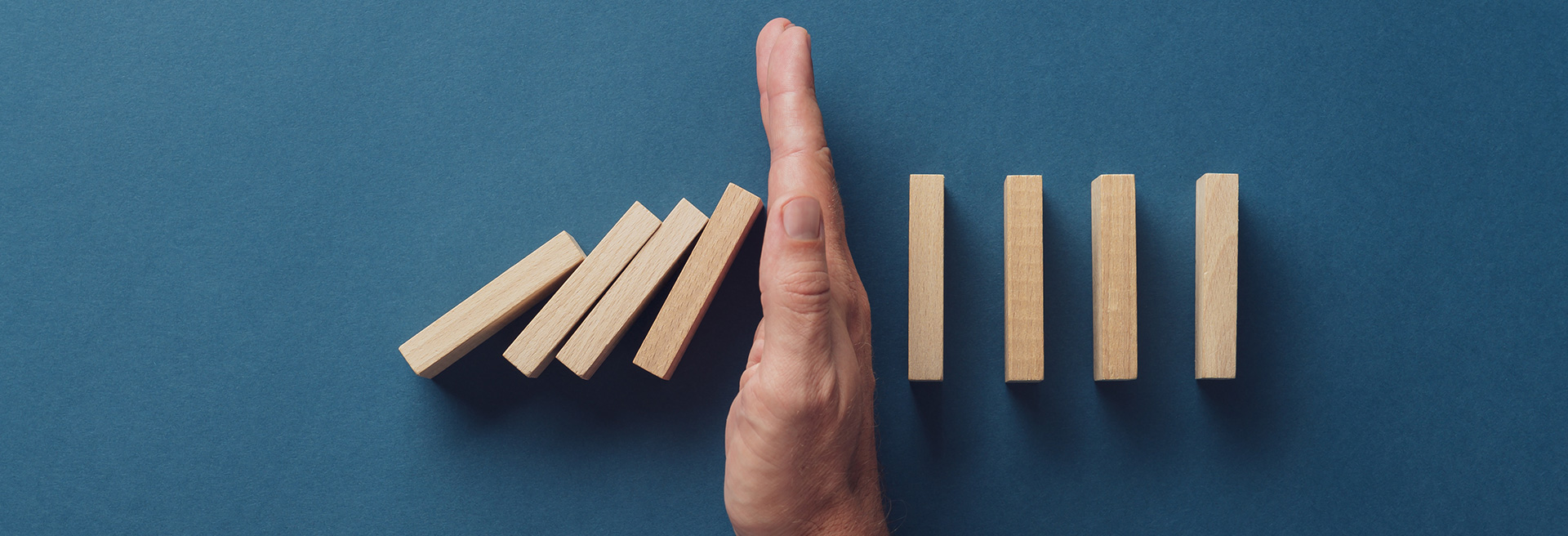 Hand stopping dominoes from falling, blue background.