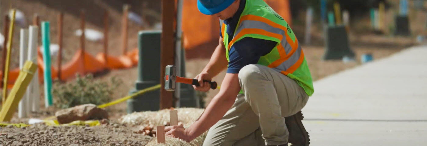 Worker pounding a wooden stake into a small roll of hay to prevent water runoff.