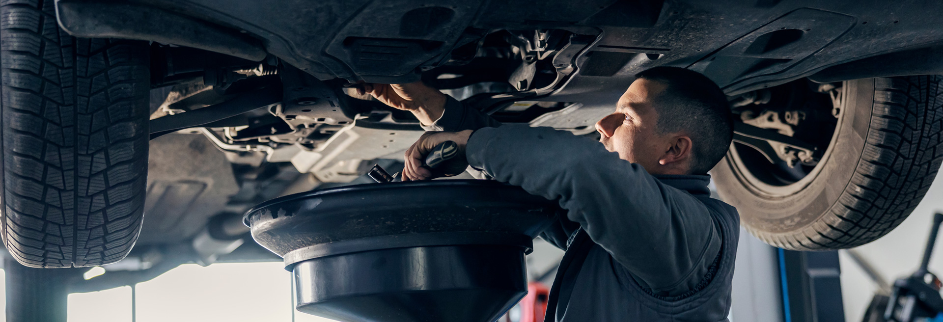 Mechanic working underneath a car, draining the engine oil into a receptacle.