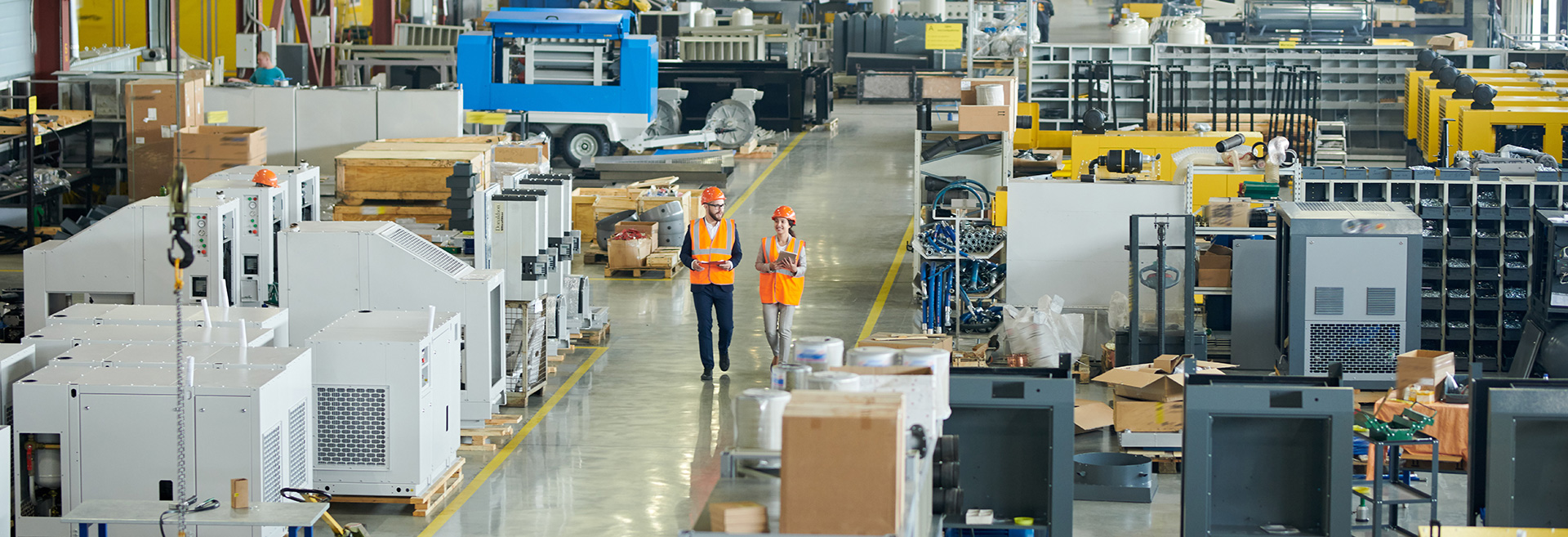 Warehouse filled with shelving and supplies, two people walking along the floor between the shelving.