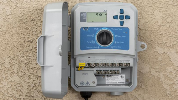 Smart irrigation controller, gray in color, mounted to a tan wall.