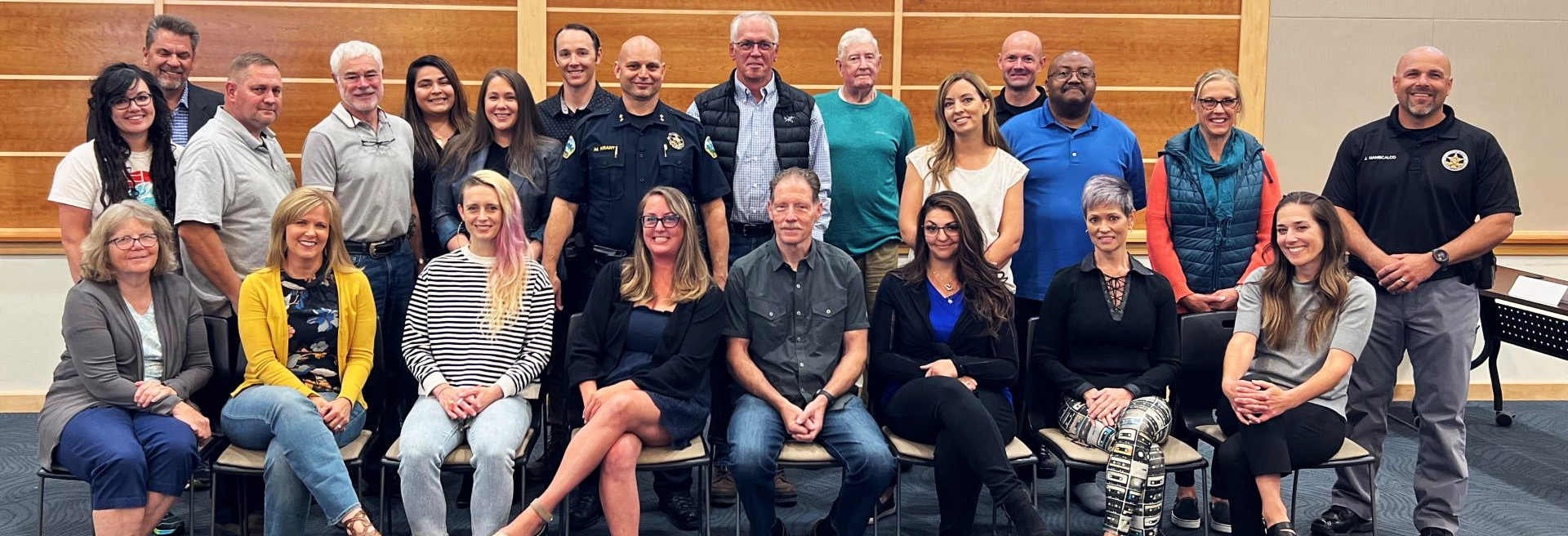 Diverse group of individuals sitting inside a well lit room with wooden paneling on the wall behind them. 