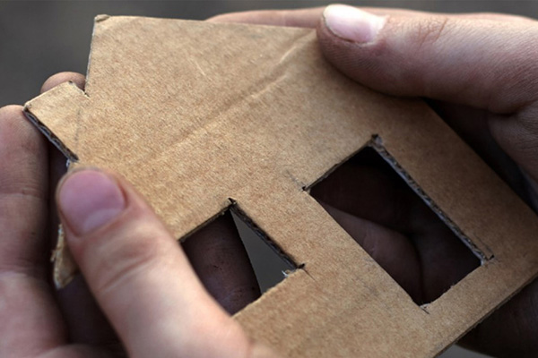 Hands holding a cardboard cutout of a house.